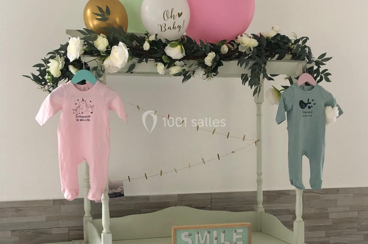 Deux grenouillères suspendues, rose et verte, décorées avec des fleurs, ballons et une pancarte ’Smile’.