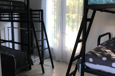 Chambre avec lits superposés, grandes fenêtres laissant entrer la lumière naturelle et parquet clair.