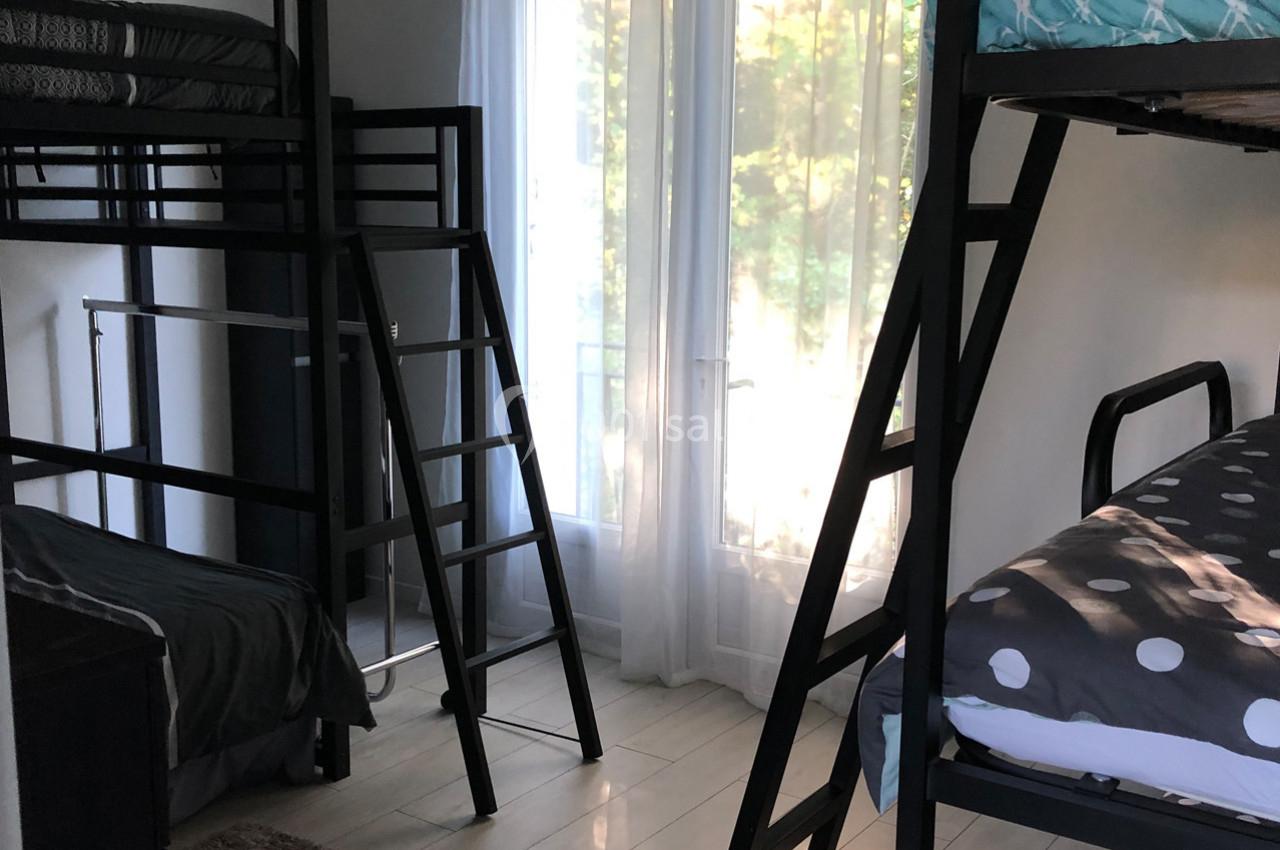 Chambre avec lits superposés, grandes fenêtres laissant entrer la lumière naturelle et parquet clair.