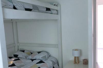 Chambre avec lits superposés, grandes fenêtres laissant entrer la lumière naturelle et parquet clair.