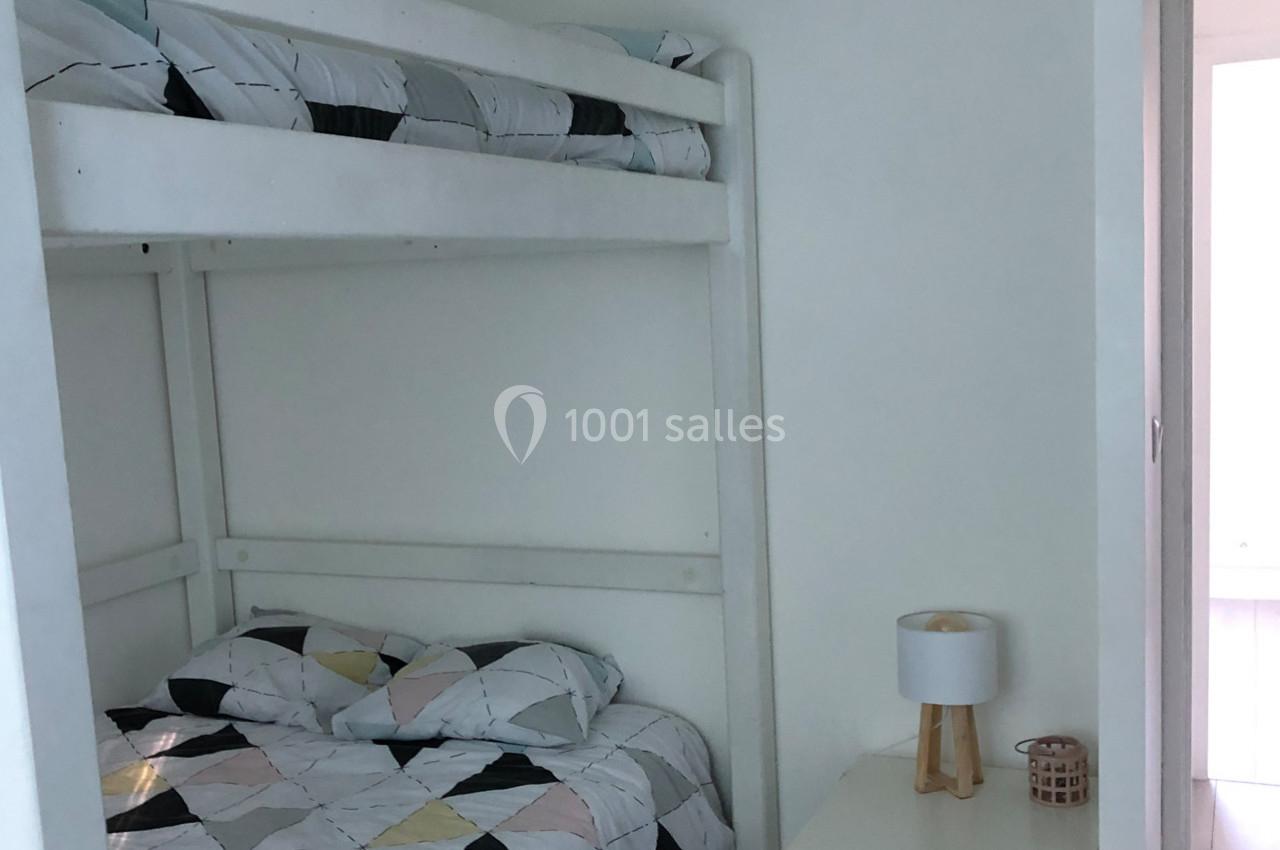 Lit superposé blanc avec linge de lit géométrique, table de chevet avec lampe et bougie dans une chambre lumineuse.