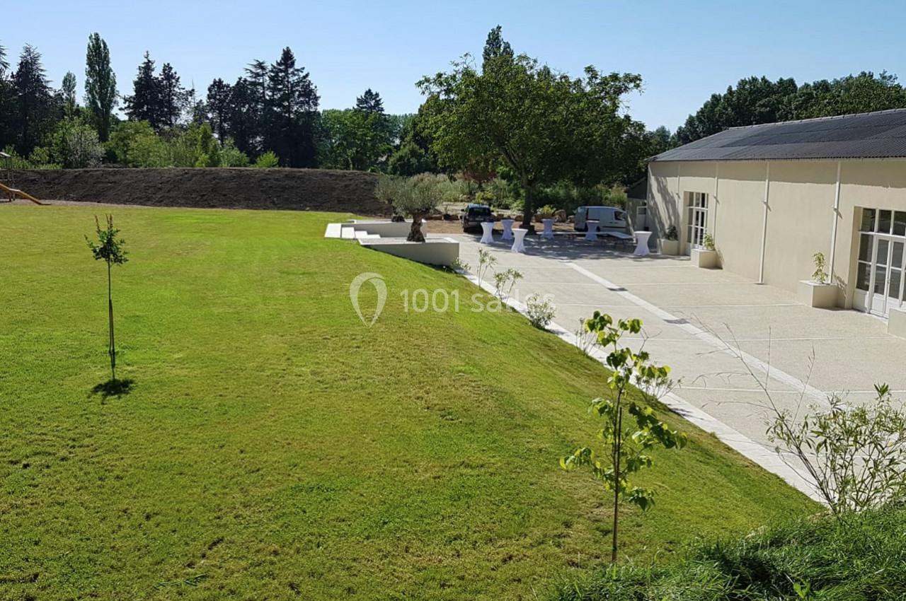 Pelouse bien entretenue bordant une terrasse avec des arbres et un bâtiment clair sous un ciel dégagé.