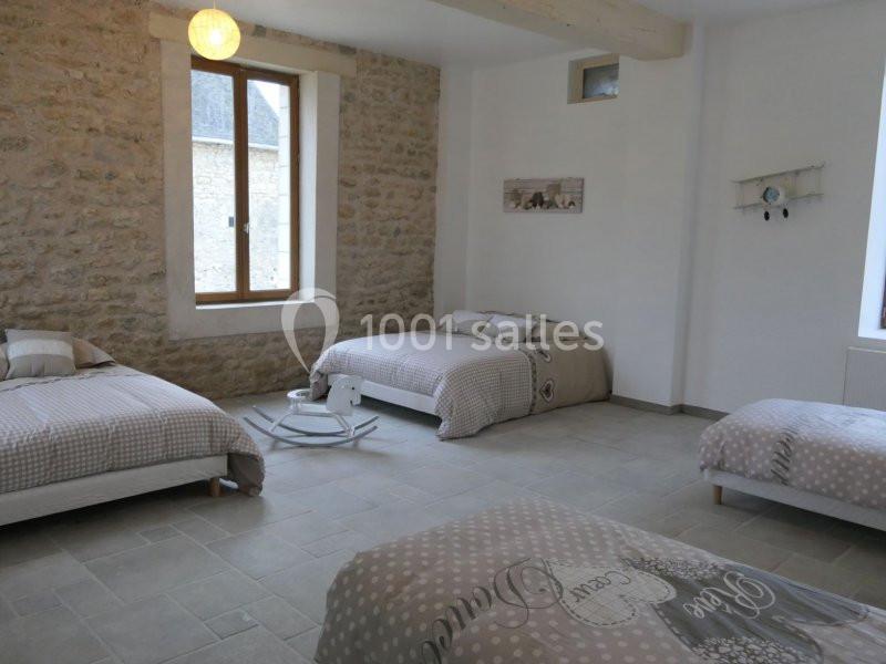 Chambre lumineuse avec murs en pierre, trois lits simples, un lit double, et une fenêtre donnant sur l'extérieur.