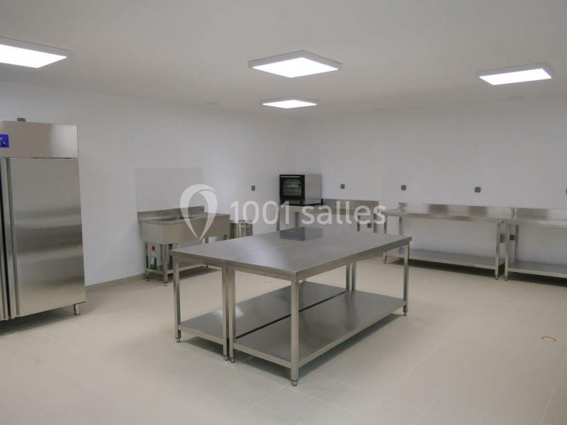 Cuisine professionnelle équipée de plans de travail en inox, d'un réfrigérateur et d'un four encastré.