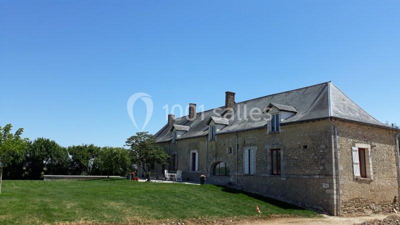 Maison en pierre avec toit en ardoise, entourée d'un jardin verdoyant sous un ciel bleu clair.