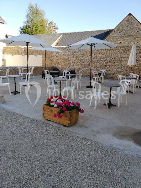 Terrasse extérieure avec tables, chaises blanches, parasols et jardinière de fleurs, entourée de murs en pierre.