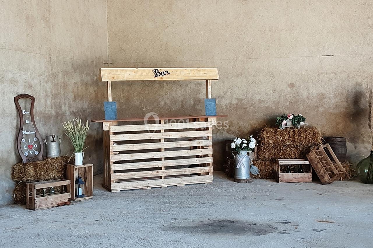 Bar en palettes en bois dans un décor rustique avec bottes de paille, fleurs et accessoires champêtres.