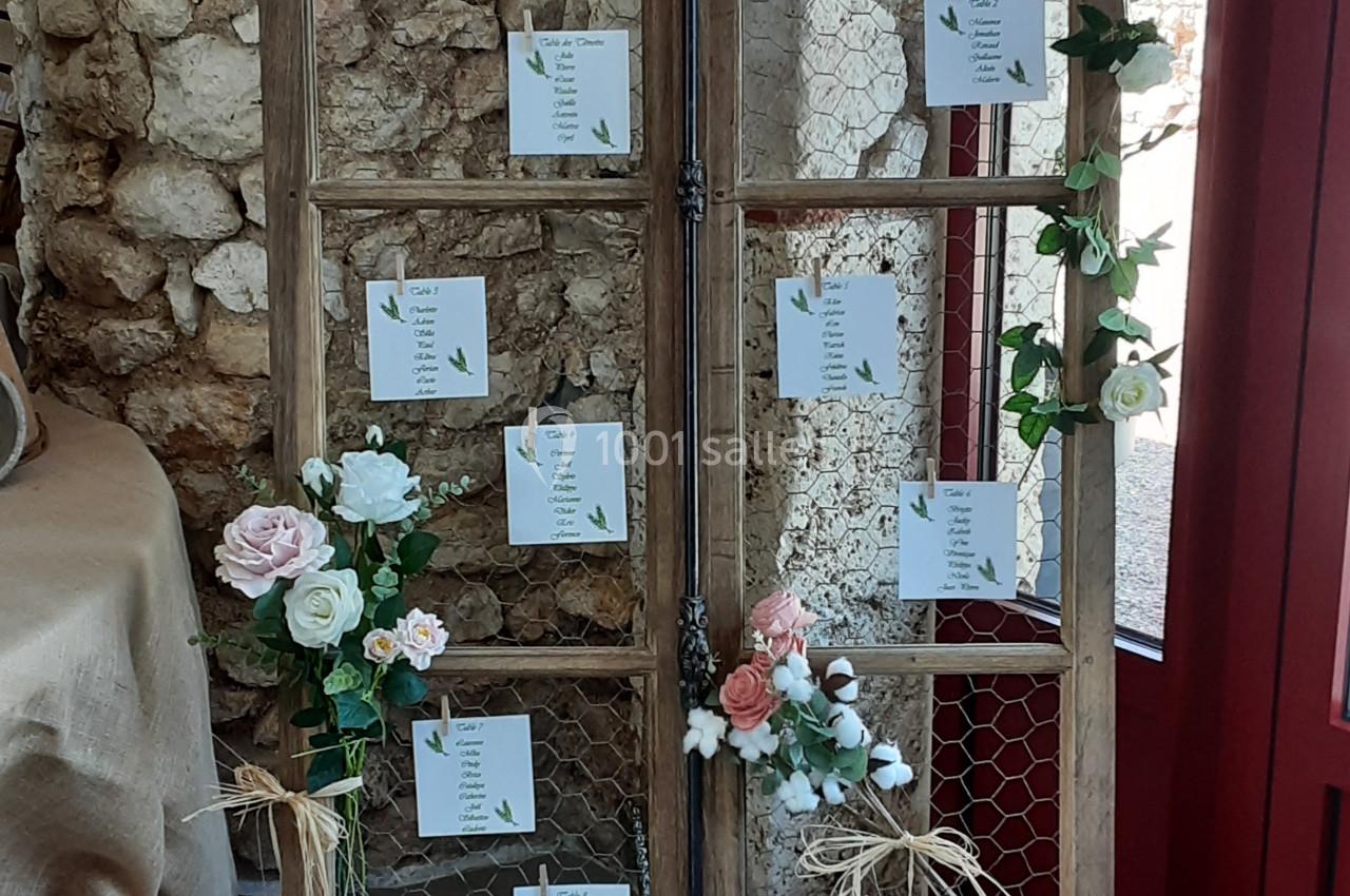 Un plan de table de mariage sur une structure en bois décorée de fleurs et de feuillages, placé près d'un mur en pierre.