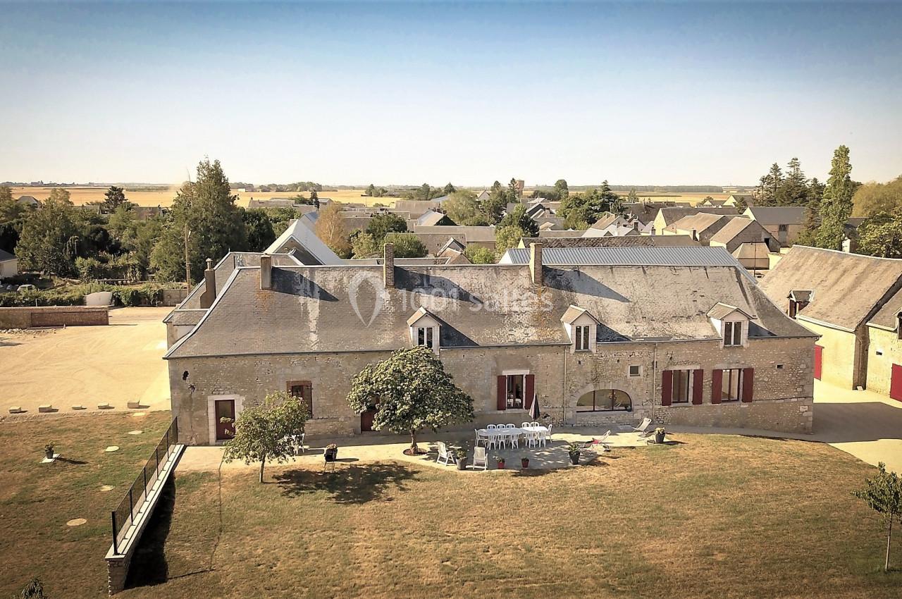 Vue aérienne d'un grand bâtiment en pierre avec des volets rouges, entouré d'arbres et d'un espace vert.