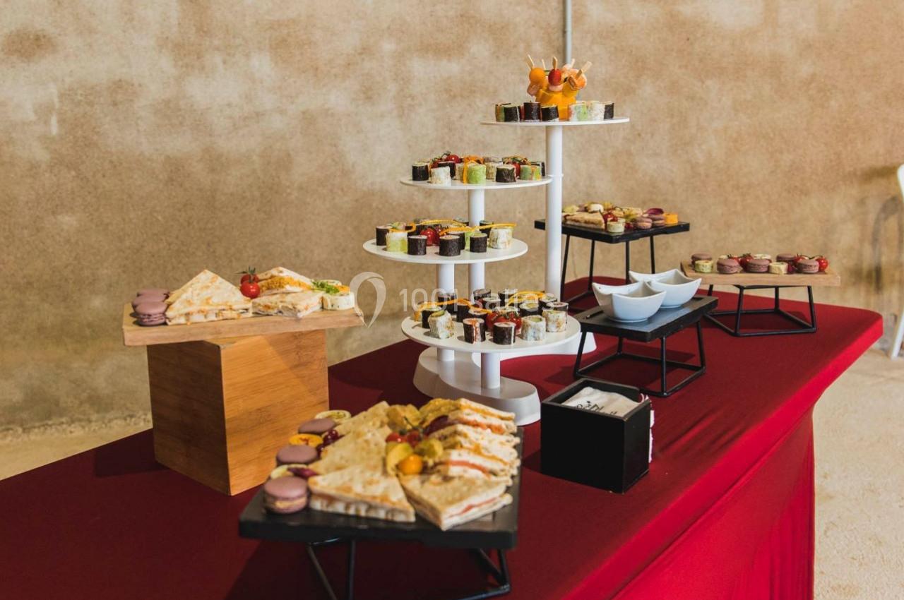 Buffet avec divers plats et desserts disposés sur une nappe rouge dans un espace intérieur sobre.