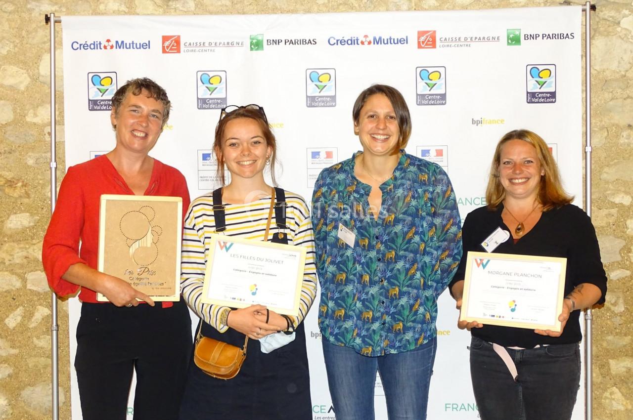 Quatre femmes souriantes posent avec des diplômes et un trophée devant un mur avec des logos d'entreprises.