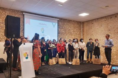 Un groupe de personnes sur scène lors d'une remise de prix dans une salle avec un mur en pierre et un écran de projection.