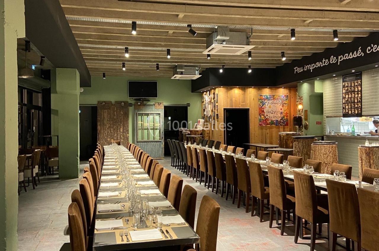 Salle de restaurant spacieuse avec de longues tables dressées, éclairage suspendu et décoration chaleureuse.