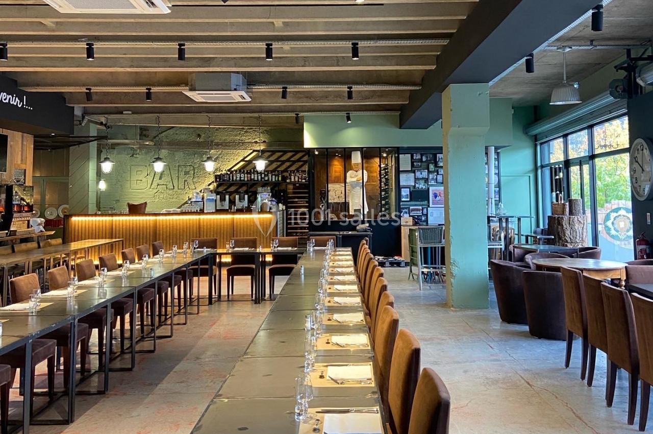 Salle de restaurant moderne avec de longues tables alignées, chaises en bois et lumière naturelle entrant par de grandes…