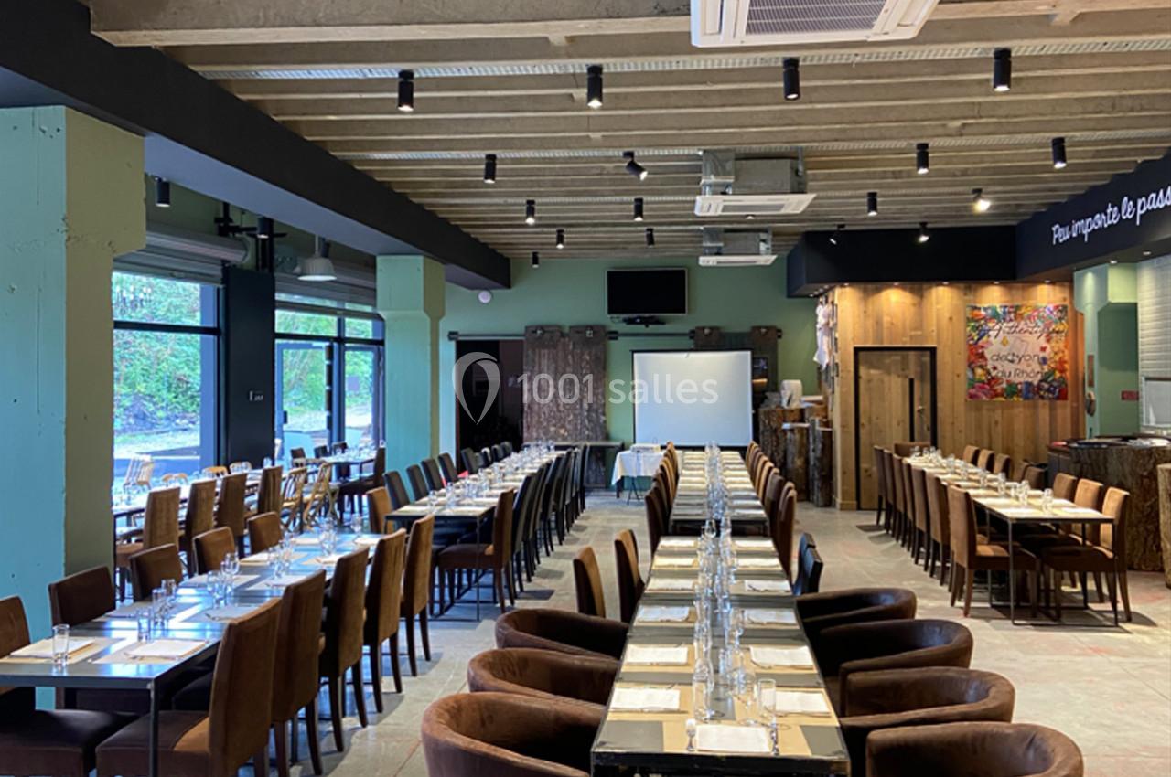 Salle de restaurant spacieuse avec de longues tables dressées, chaises en velours marron et éclairage moderne.