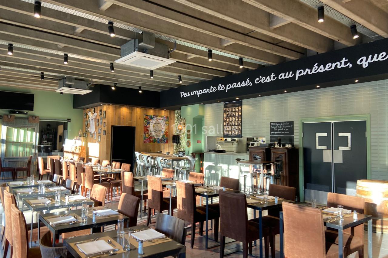 Salle de restaurant lumineuse avec tables dressées, chaises en cuir marron et décoration murale éclectique.