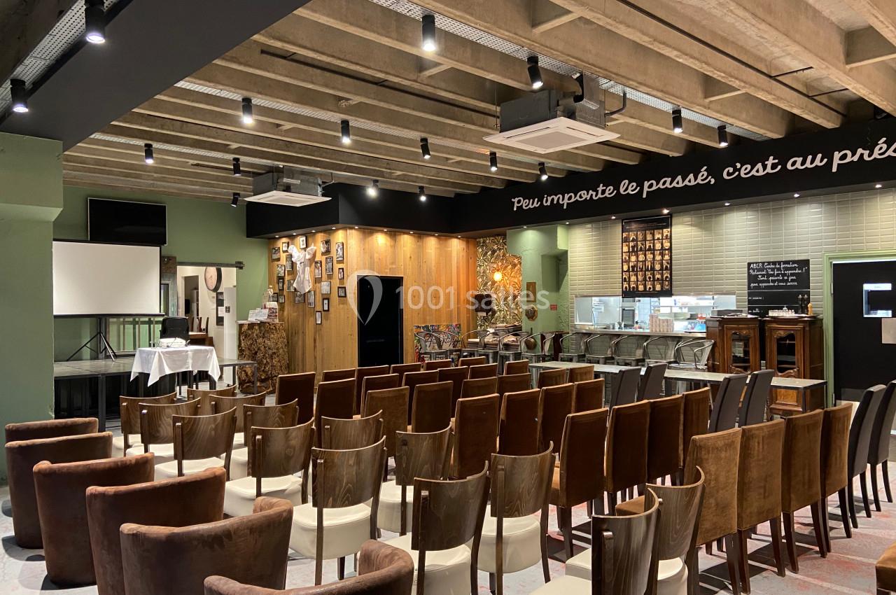 Salle aménagée avec des rangées de chaises, un écran de projection, et un espace décoré avec des cadres et des panneaux…