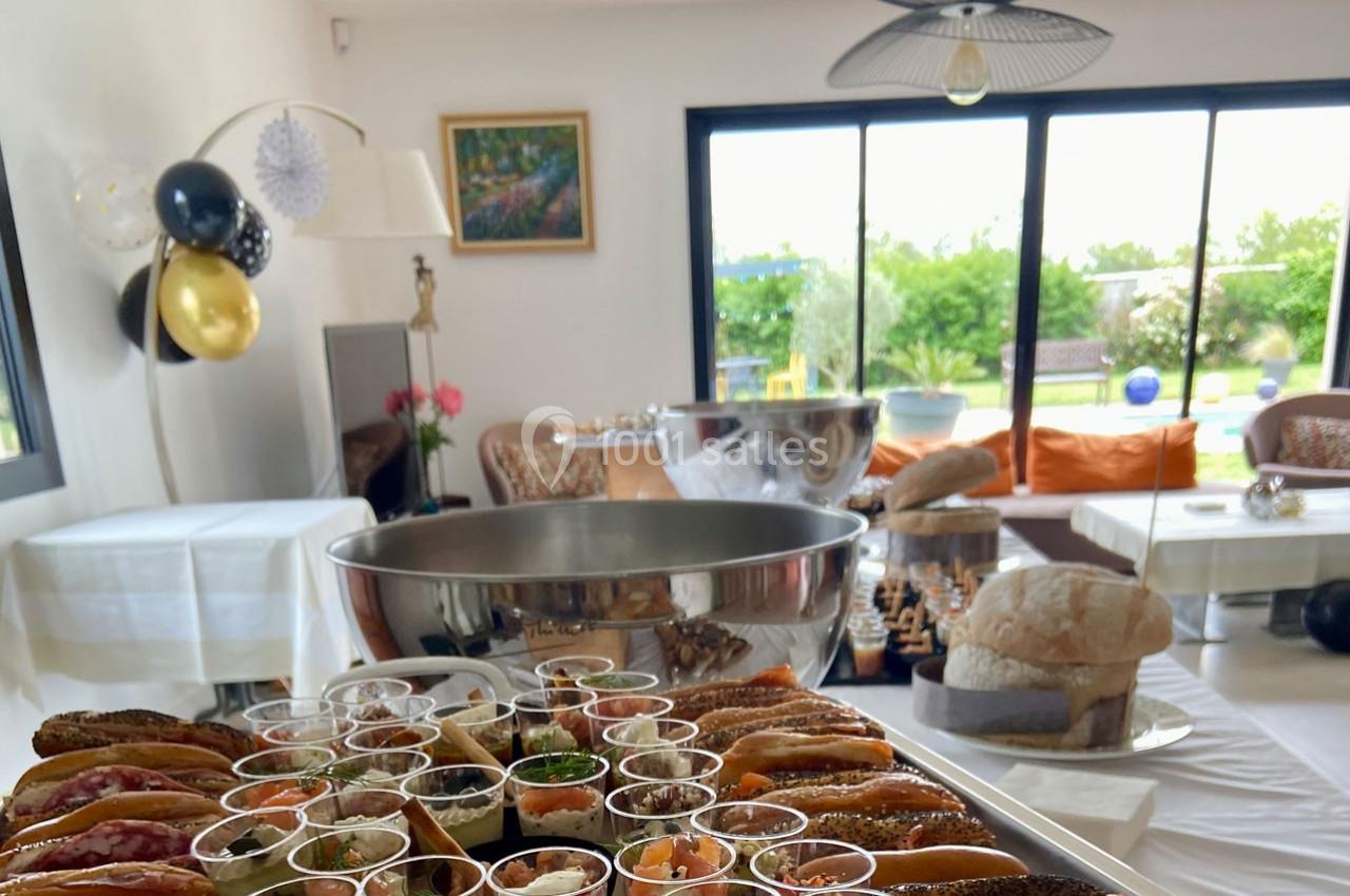 Buffet avec assortiments de verrines, pains et amuse-bouches dans une salle lumineuse avec vue sur un jardin.