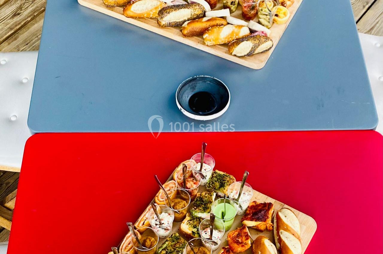 Plateaux de tapas variés avec verrines, toasts et amuse-bouches, présentés sur des tables rouge et grise.