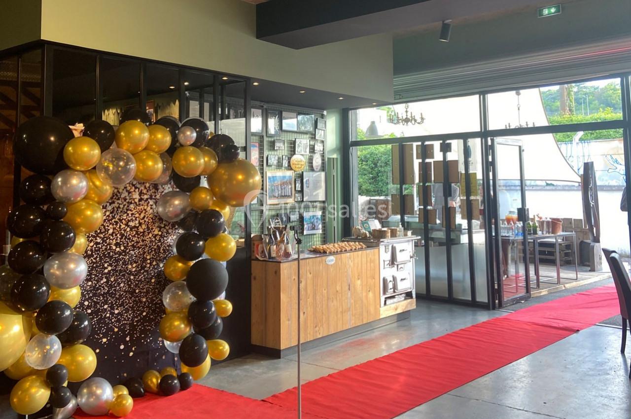 Décoration festive avec arche de ballons noirs et dorés, tapis rouge et vue sur une terrasse extérieure.