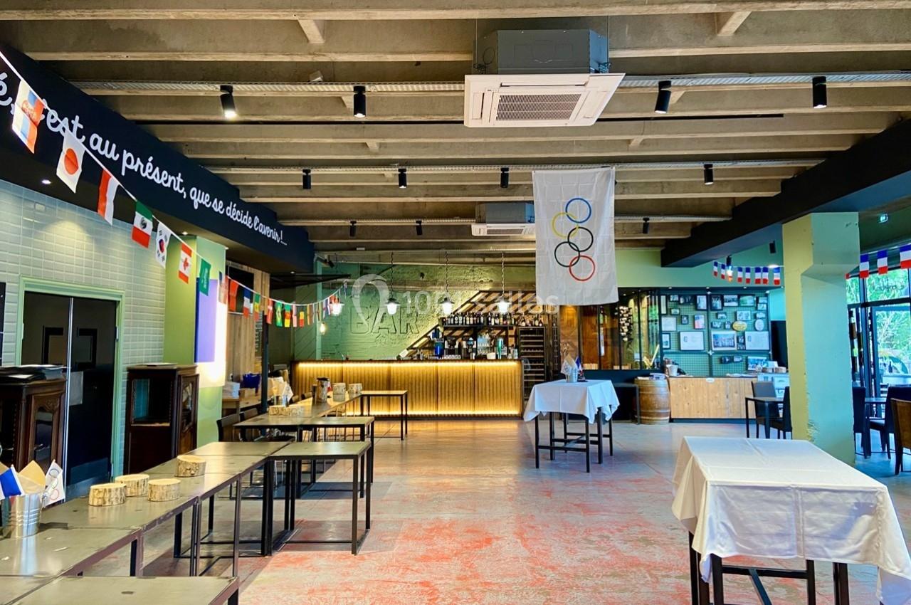 Salle de restaurant décorée de drapeaux internationaux, avec un bar éclairé en arrière-plan et des tables dressées.