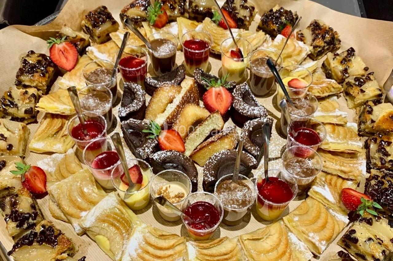 Plateau de desserts variés avec parts de gâteaux, tartes aux fruits, verrines et fraises fraîches en décoration.