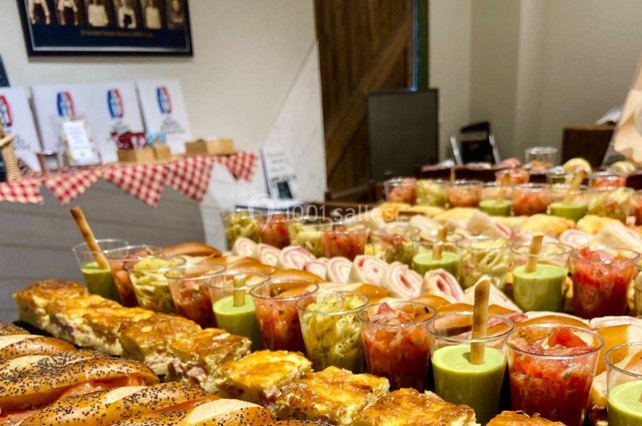 Buffet varié avec verrines colorées, quiches, roulés et pains garnis disposés sur une table en intérieur.