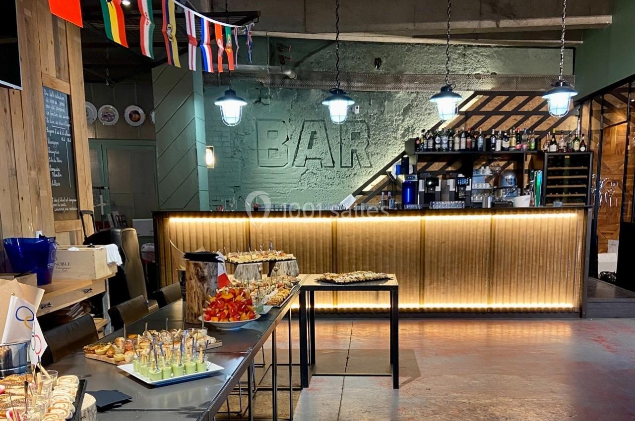 Buffet avec verrines et amuse-bouches devant un bar éclairé, décoré de drapeaux internationaux suspendus.