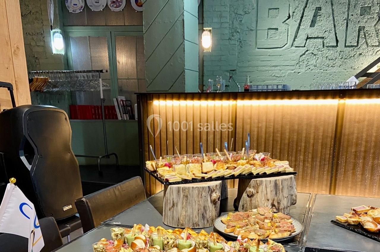 Buffet composé de verrines, toasts et amuse-bouches, disposé sur une table dans un espace au décor industriel.