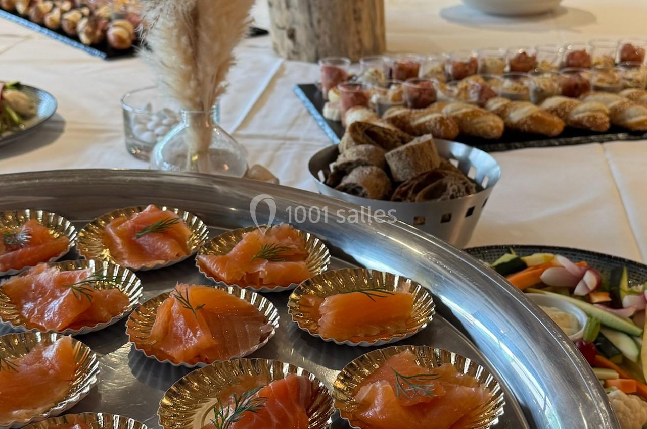 Plateau de tranches de saumon fumé décorées d'aneth, entouré de pains, légumes et amuse-bouches sur une table.