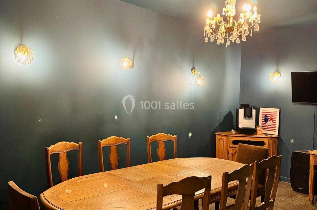 Salle à manger avec table en bois, chaises assorties, mur bleu, lustre, appliques murales et machine à café sur un meuble.