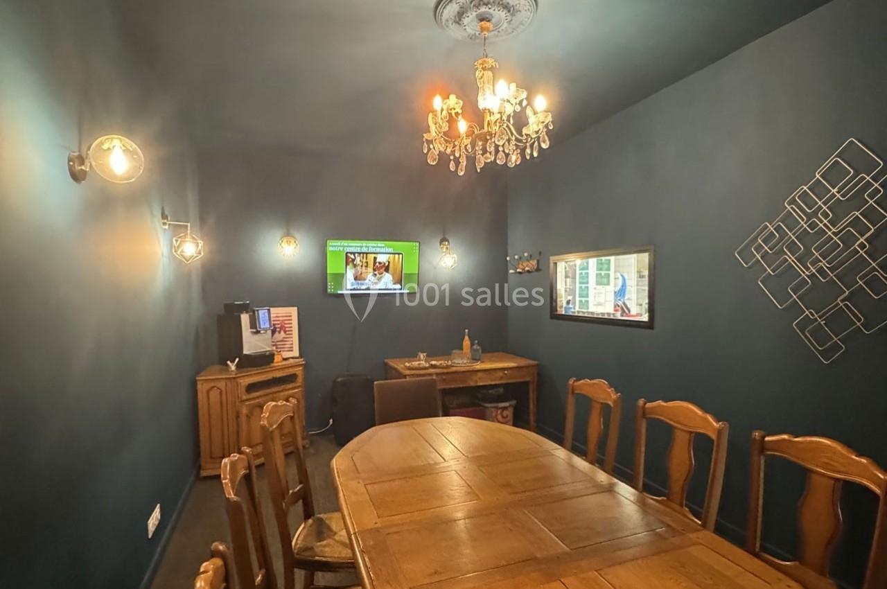 Salle à manger avec murs bleu foncé, table en bois, chaises assorties, lustre et écran mural allumé.