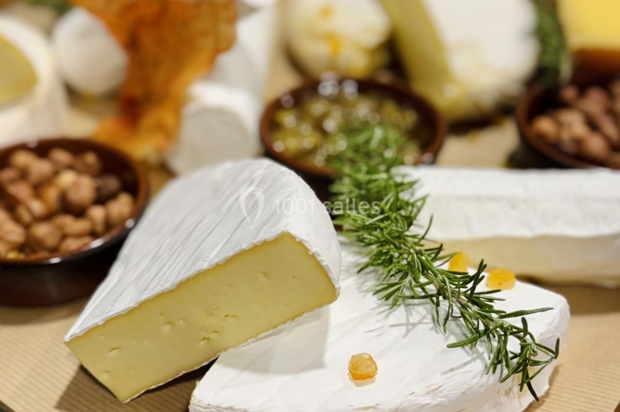 Assortiment de fromages à pâte molle avec garnitures, herbes fraîches et accompagnements en arrière-plan.