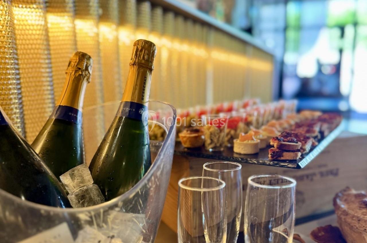 Bouteilles de champagne dans un seau à glace avec des verres et un buffet de bouchées apéritives en arrière-plan.