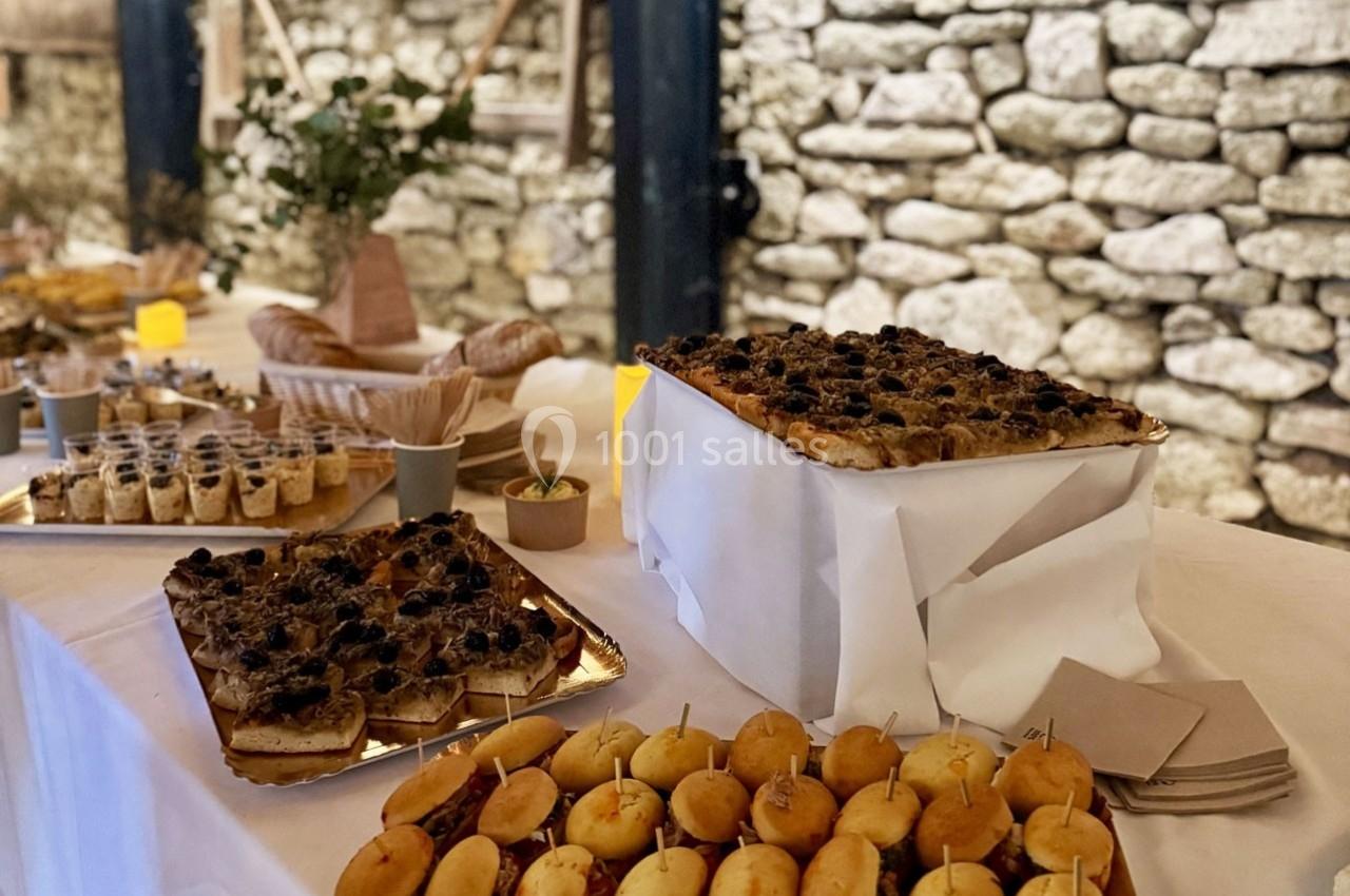 Buffet avec divers plats, dont des mini-sandwichs et des tartes salées, disposés sur une table dans un cadre en pierre.