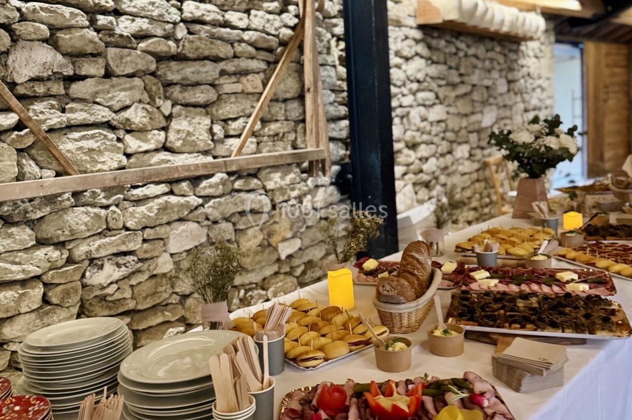 Buffet varié avec charcuteries, pains, légumes et desserts, disposé sur une table devant un mur en pierre.