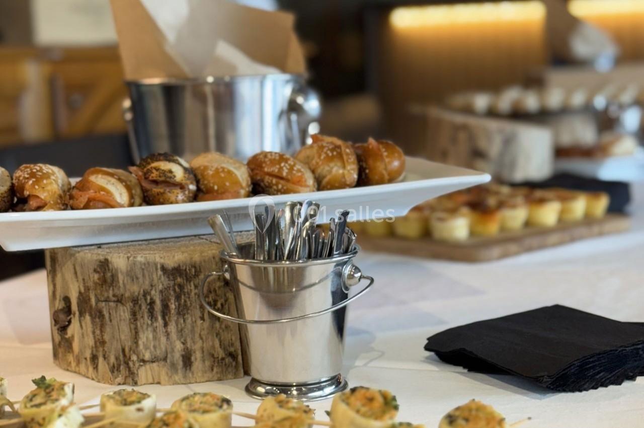 Plateau de viennoiseries salées et mini-quiches disposé sur une table avec des couverts dans un seau en métal.
