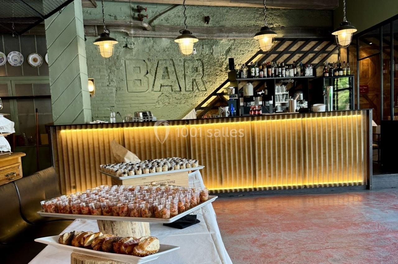 Buffet avec viennoiseries, verrines et sushis devant un bar éclairé dans un espace au style industriel.