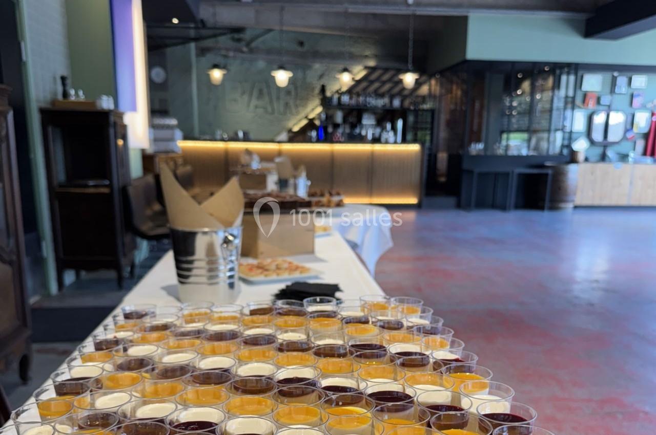 Buffet avec des verrines colorées en premier plan, dans une salle avec un bar en arrière-plan.
