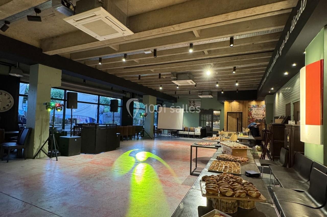 Salle spacieuse avec tables garnies de viennoiseries, éclairage tamisé et espace libre pour des événements.
