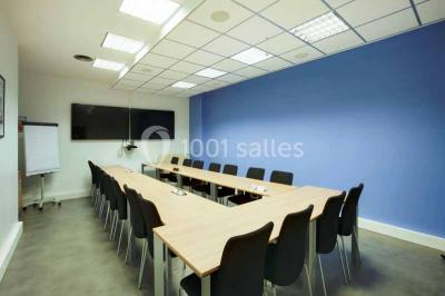 Salle de réunion avec table en bois, chaises noires, mur rouge décoré et écran mural éteint.