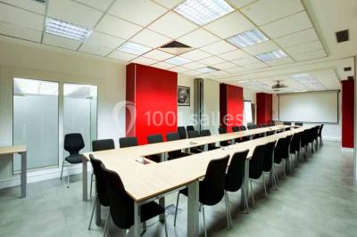 Salle de réunion avec table en bois, chaises noires, mur rouge décoré et écran mural éteint.