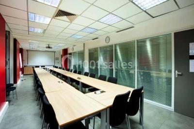 Salle de réunion avec table en bois, chaises noires, mur rouge décoré et écran mural éteint.