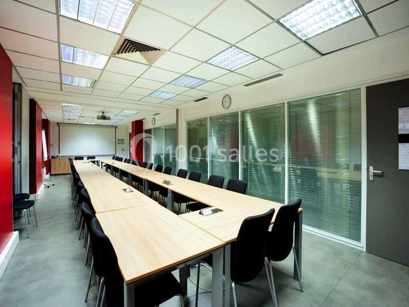 Salle de réunion lumineuse avec de longues tables en bois, des chaises noires et un tableau blanc au fond.