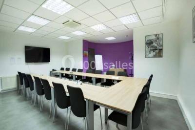 Salle de réunion avec table en bois, chaises noires, mur rouge décoré et écran mural éteint.