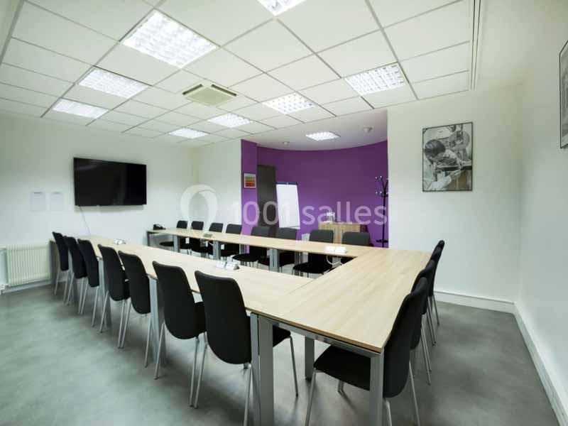 Salle de réunion moderne avec une grande table en U, des chaises noires, un écran mural et un tableau blanc.