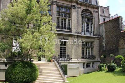 Salle de réunion avec table en bois, chaises noires, mur rouge décoré et écran mural éteint.