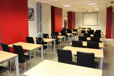 Salle de réunion avec table en bois, chaises noires, mur rouge décoré et écran mural éteint.