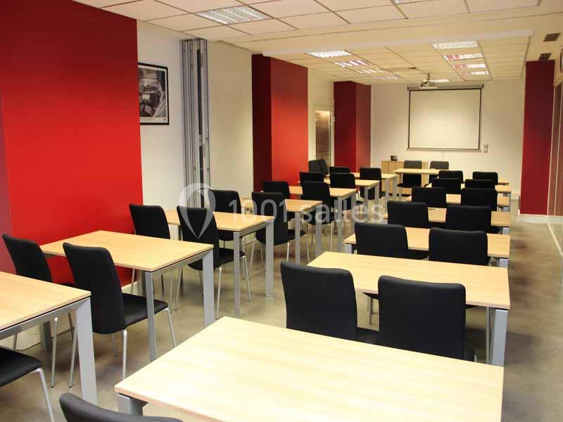 Salle de classe moderne avec des tables en bois, des chaises noires et un projecteur au fond.