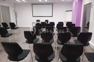 Salle de réunion avec table en bois, chaises noires, mur rouge décoré et écran mural éteint.